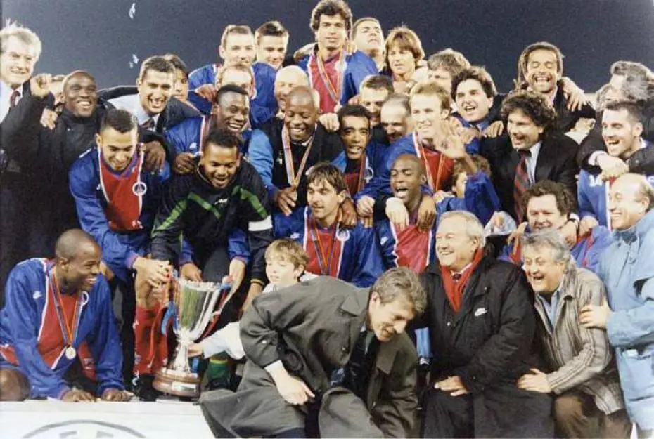 Les joueurs du Paris Saint-Germain célébrant leur victoire en Coupe des Coupes 1996, entourés du staff, avec le trophée brandi au centre du groupe.