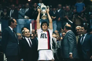 Dominique Bathenay brandit la Coupe de France 1982 lors de la première victoire majeure du Paris Saint-Germain, entouré d’officiels et de supporters au Parc des Princes.
